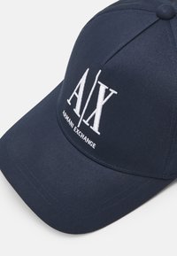 Cappellino da baseball blu realizzato in tessuto misto cotone, con logo ricamato bianco "A/X" e "ARMANI EXCHANGE" sul fronte. Visiera curva.