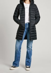 Svart pufferjacka med huva, quiltad design, framknäppning, två sidofickor. Kombinerad med ljusblå jeans och svarta sneakers.