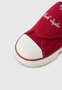 Κόκκινο πάνινο αθλητικό παπούτσι με λευκή λαστιχένια μύτη, διαθέτει ελαστικό κλείσιμο και ραμμένη σχεδίαση. Λογότυπο «Chuck Taylor» στο πλάι.