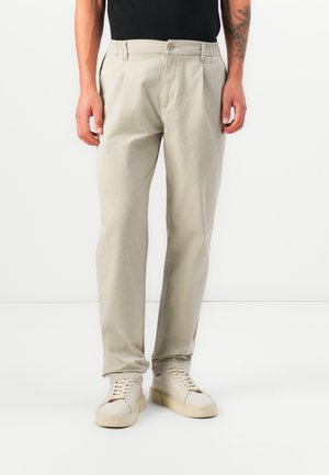 Pantalons en coton beige clair présentant une coupe décontractée, une taille élastique et une fermeture à bouton avant, associés à des baskets crème.