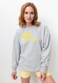 Grauer Sweatshirt mit gelbem "elko Freestyle" Grafik, lockere Passform, runder Halsausschnitt, weiche Textur, kombiniert mit gelben, gerippten Shorts mit hohem Taillenbund.