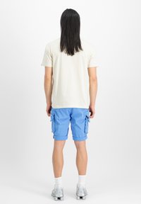 Lys beige kortærmet t-shirt og blå cargo shorts med flere lommer, parret med hvide sokker og sølvfarvede løbesko.