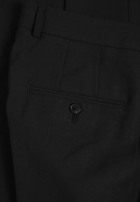 Pantalones negros con frente plano, un bolsillo trasero con cierre de botón y tejido texturizado. Diseño simple y ajustado.