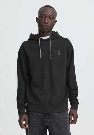 Sweat-shirt à capuche noir avec une finition texturée, cordons de serrage et un accent logo. Associé à un jean gris foncé déchiré.