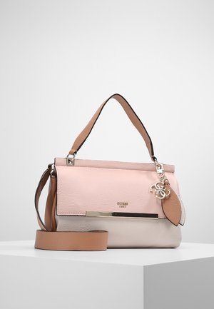 Sac à main doux rose et beige avec poignées et bandoulière couleur camel, décoré d’une barre métallique et d’un charme décoratif, posé sur une surface blanche.