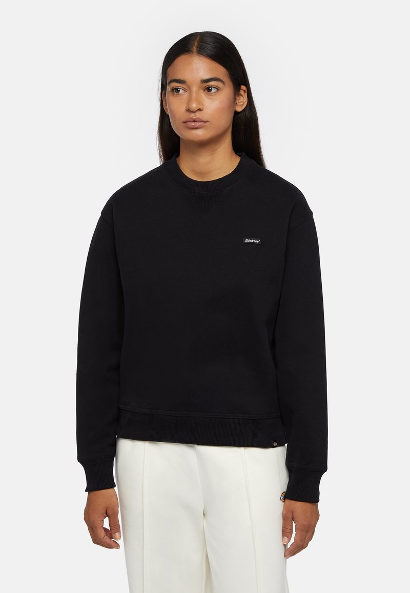 Svart sweatshirt med rund halsringning, ribbad mudd och nederkant; har en liten logotyp på bröstet och en mjuk, texturerad yta.