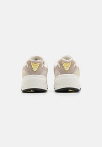 Beżowo-kremowe sneakersy z zamszową i siateczkową cholewką, z żółtym akcentem na pięcie, gumową podeszwą i wyściełanym kołnierzem.