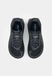Chaussures de trail running noires avec un dessus texturé, des accents réfléchissants et des lacets à motifs. Elles possèdent une semelle rembourrée et des trous de ventilation hexagonaux.