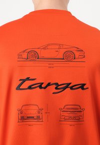 Oranžs kokvilnas T-krekls ar melnu līniju zīmējumiem par automašīnu, kurai ir izmēri, un vārds "targa" izšūts melnā krāsā aizmugurē.