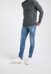 Harmaan neuloksen villapaita, jossa on korkea kaula-aukko, yhdistettynä vaaleansinisiin farkkuihin ja valkoisiin tennareihin, joissa on mustia yksityiskohtia.