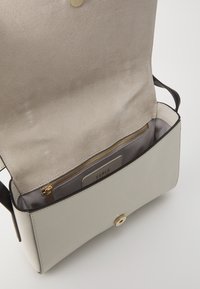 Ljusgrå läderhandväska med en slät yta, som har en guldfärgad tryckknappsstängning och ett innerfack med dragkedja, som framhäver rena linjer och funktionell design.