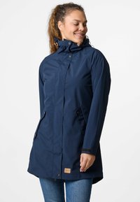 Parka impermeabile blu navy con colletto alto, chiusura anteriore con bottoni a pressione e tasche laterali. Presenta dettagli in legno e una vestibilità rilassata.