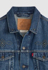 Denim jacket met een klassieke snit, blauwe kleur, metalen studsaccenten aan de voorkant en een leren label aan de binnenkant met merkinformatie.