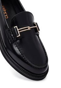 Mocassino in pelle nera con una finitura liscia, dotato di una fibbia dorata e di un'accurata cucitura lungo il bordo della suola.