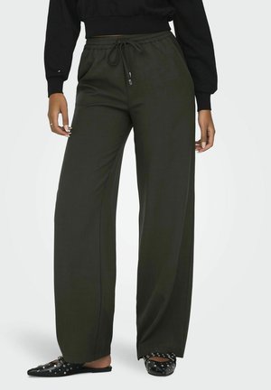 Pantaloni a gamba larga in tessuto verde scuro con finitura texture, dotati di una vita elastica e lacci. Indossati con ciabatte nere con borchie.