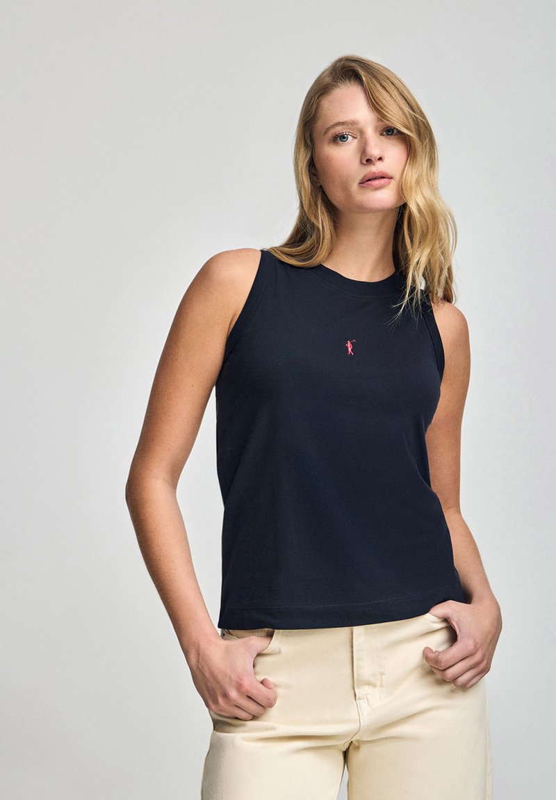 Czarny bezrękawnik wykonany z bawełny, z okrągłym dekoltem i małym czerwonym logo na klatce piersiowej. W zestawieniu z jasnymi spodniami.