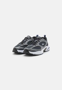 Scarpe sportive con tomaia in mesh grigia e accenti neri. Suola intermedia bianca spessa, suola esterna nera texturizzata e puntale rinforzato.