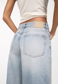 Světle modré džínové kalhoty s volným střihem, se zadními kapsami a jednoduchou koženou nášivkou na pásku. Měkká textura a vybledlý vzor.