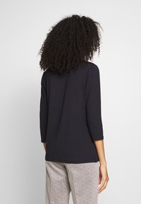 Schwarzes Langarmshirt mit lockerer Passform und Rundhalsausschnitt. Weicher Stoff, minimalistisches Design und leicht längerer Saum hinten.