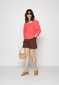 Top coral de mangas bufantes com detalhe de franzido, calções castanhos, mala bege e sandálias de salto bloco em tom de pele com design recortado.