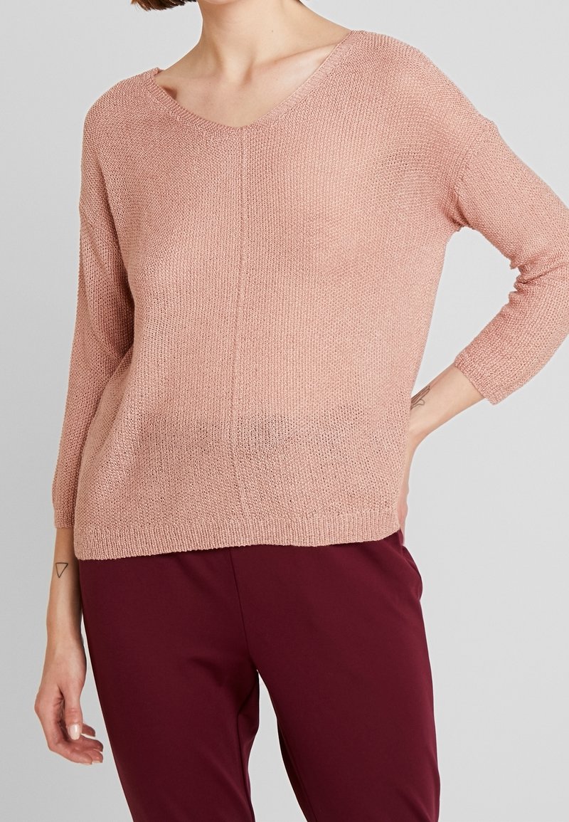Pull en maille rose clair avec un col en V et des manches trois-quarts. Présente une coupe décontractée et un tissu texturé. Assorti à un pantalon bordeaux.