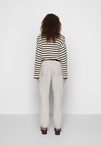 Suéter riscado em preto e branco com um design cropped, combinado com calças largas em bege claro e sapatos de plataforma pretos.