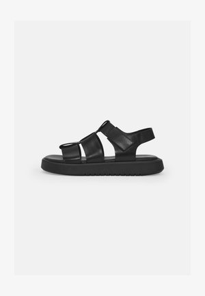 Black sandals with multiple adjustable straps, flat sole, and textured rubber base. Smooth leather finish with a minimalist design.
