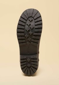 Zwarte rubberen zool met een diep profiel en logo, met meerdere kruis- en lijnontwerpen voor grip. Soepele, gelijkmatige textuur.