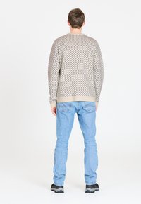 Beige trui met een stippenpatroon, ruime pasvorm en geribbelde boorden, gecombineerd met lichtblauwe spijkerbroek en zwarte sneakers, gezien vanaf de achterkant.