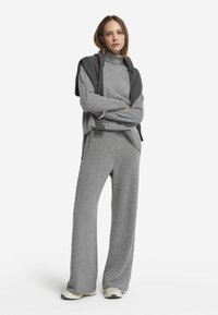 Pull en tricot gris à col haut, superposé avec un châle gris foncé. Associé à un pantalon gris à jambes larges avec un détail texturé sur le côté.