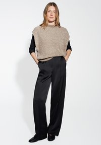 Top senza maniche a maglia beige con collo alto, abbinato a pantaloni neri a gamba larga. Tessuto morbido con una vestibilità comoda e tasche laterali.
