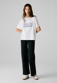 T-shirt en coton blanc avec un graphisme "Red Bull Racing", associé à un jean large noir et des baskets blanches.