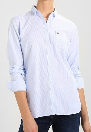 Camisa de botones a rayas azul claro y blanca con un bolsillo en el pecho izquierdo y mangas remangadas. Fabricada en un tejido suave y texturizado.