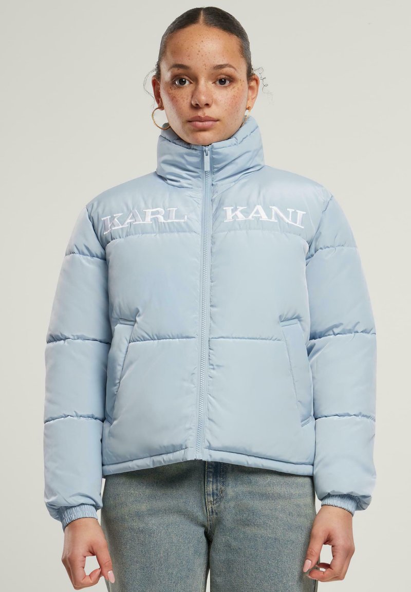 Lysblå pufferjakke med høj hals, frontlynlås og broderet logo. Har elastiske manchetter og sidelommer. Kort cropped design.