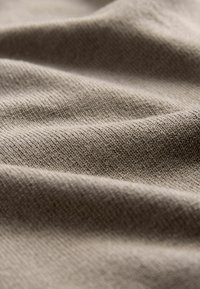 Beige stof met een structuur van geribbelde patronen, met zachte plooien en kreukjes die zachtheid en een subtiele glans benadrukken.