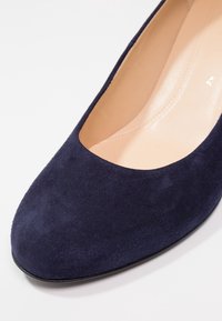 Gros plan d'une chaussure plate pour femme en daim bleu marine avec un bout rond et une doublure intérieure beige sur fond blanc.