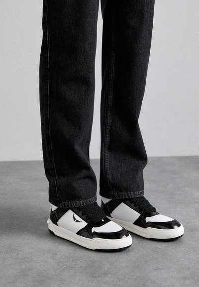 Jean en denim noir associés à des baskets blanches et noires avec une finition texturée, des lacets prononcés et un détail de logo sur le côté.