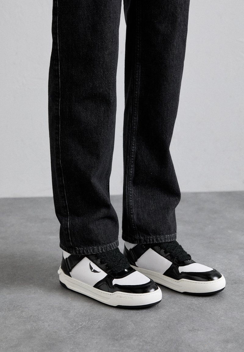 Black denim jeans paired with white and black sneakers featuring a textured finish, prominent lacing, and a logo detail on the side.