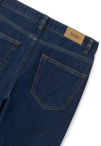 Jeans de mezclilla de color azul oscuro con una textura suave, que cuentan con dos bolsillos traseros y una etiqueta de cuero que dice "REPÚBLICA DE MEZCLILLA" en la cinturilla.
