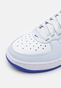 Bota branca e azul clara com biqueira perfurada, atacadores brancos, pequeno logotipo azul da Nike e borda da sola texturizada em azul.