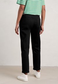 Svarta raka byxor med hög midja och uppvikta fållar, kombinerade med en grön och vit randig topp. Tyget verkar slätt och har fickor.