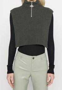 Top smanicato a coste di colore verde scuro con colletto alto e dettaglio in zip argentata, abbinato a pantaloni in ecopelle verde chiaro.