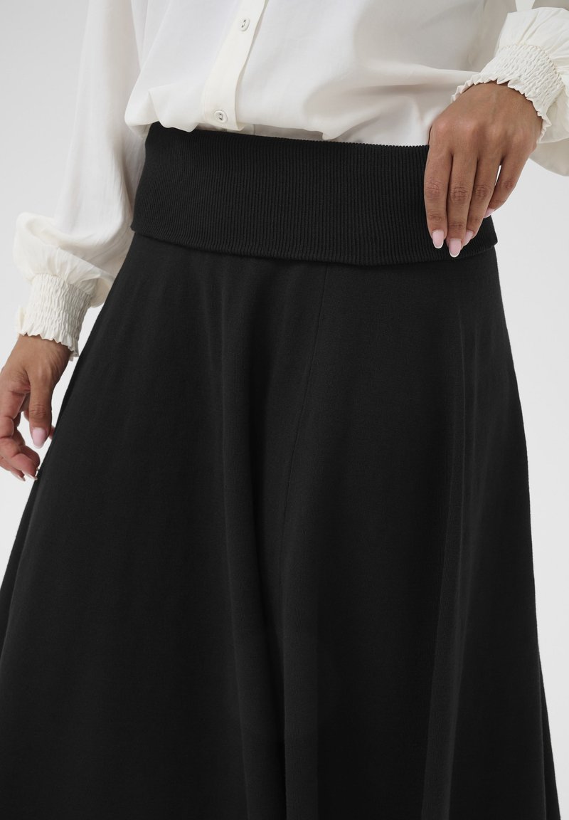Jupe midi noire avec une large ceinture côtelée. Fabriquée dans un tissu lisse, elle présente une silhouette en A et un drapé doux.