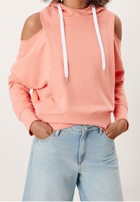 Sweatshirt pêche clair avec un design à épaules dénudées, cordons blancs et poignets côtelés, associé à un jean large bleu clair.