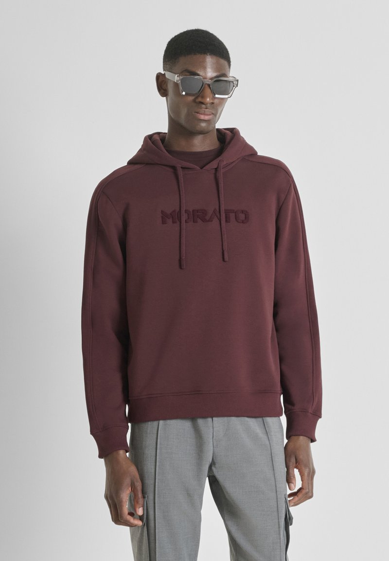 Felpa borgogna con logo testurizzato "MORATO", coulisse regolabile e polsini a coste, abbinata a pantaloni cargo grigi chiari e occhiali da sole.
