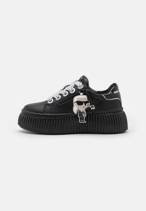 Baskets à plateforme noires avec semelle côtelée, lacets blancs à pois, œillets argentés et porte-clés figurine de dessin animé suspendu aux lacets.