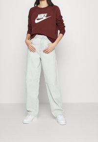 Maroon Nike sweatshirt med vitt logotyp, kombinerad med ljusblå högmidjade vida jeans och vita sneakers. Släta bomulls- och denimtexturer.