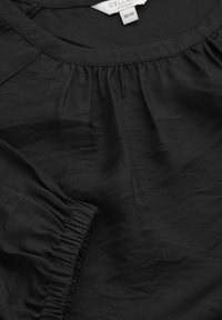 Svart blus i lätt tyg med rynkade detaljer runt halsringningen och elastiska ärmmuddar. Lappen visar storlek 38/40.