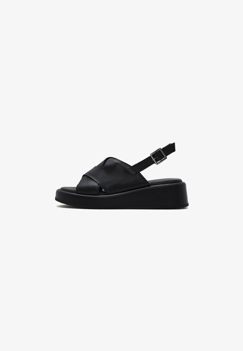 Sandalias de cuña negra con diseño de tiras cruzadas, hechas de material suave, con un cierre lateral y una suela de plataforma texturizada.