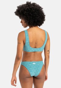 Egy két részes bikini türkiz színben, strukturált mintával. A melltartó széles pántokkal és alacsony hátrésszel rendelkezik, míg a bugyi magas vágású és logós díszítéssel ellátott.